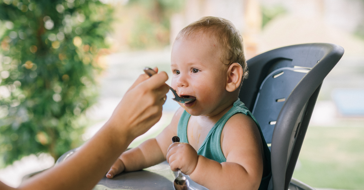 Aikuinen syöttää vauvalle kiinteää soseruokaa
