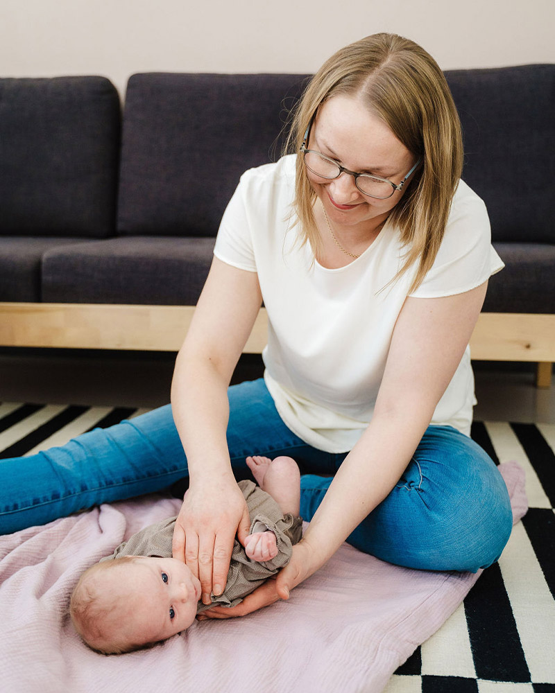 Vauva makaa lattialla viltin päällä vauvahieronnassa Kouvolassa. Hieroja käsittelee vauvaa.